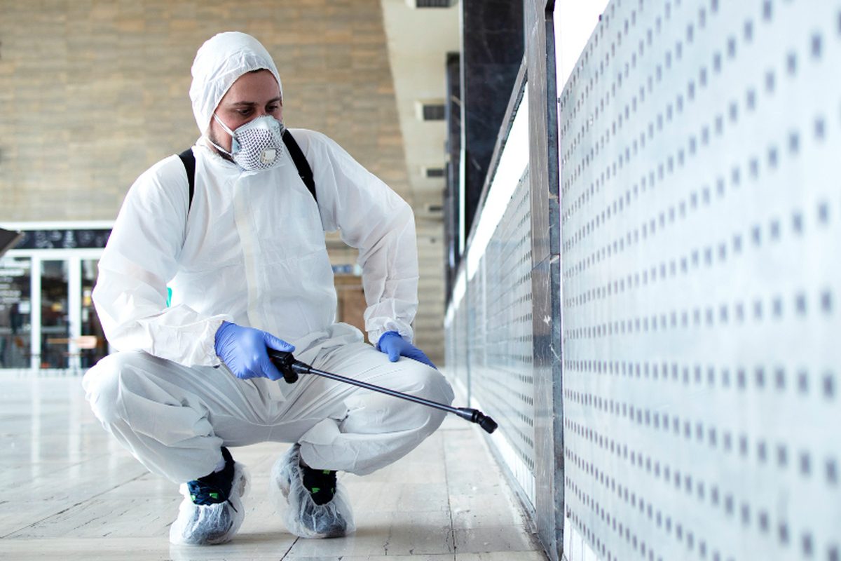 Technician in protective gear spraying mould treatment along an interior wall