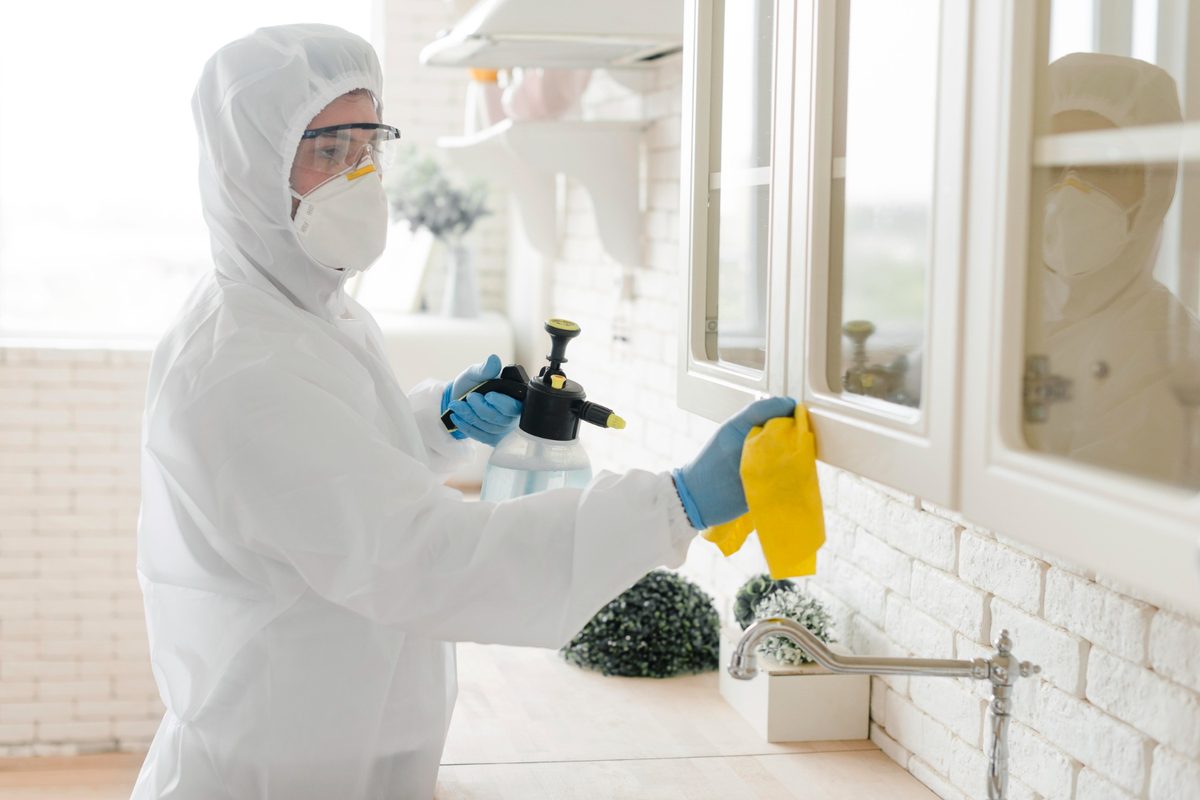 Technician in a protective suit and respirator treating mould around a window frame
